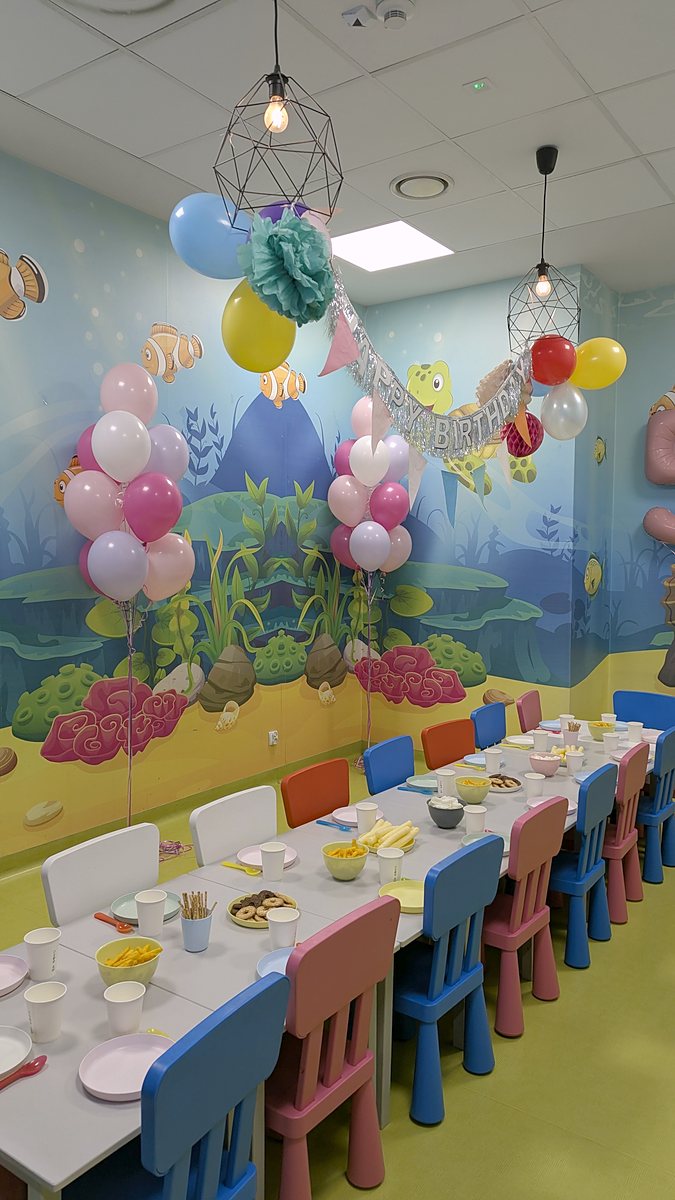 Stół urodzinowy w sali zabaw, przy nim bukiety balonów z helem w różu, fuksji, liliowym i bieli